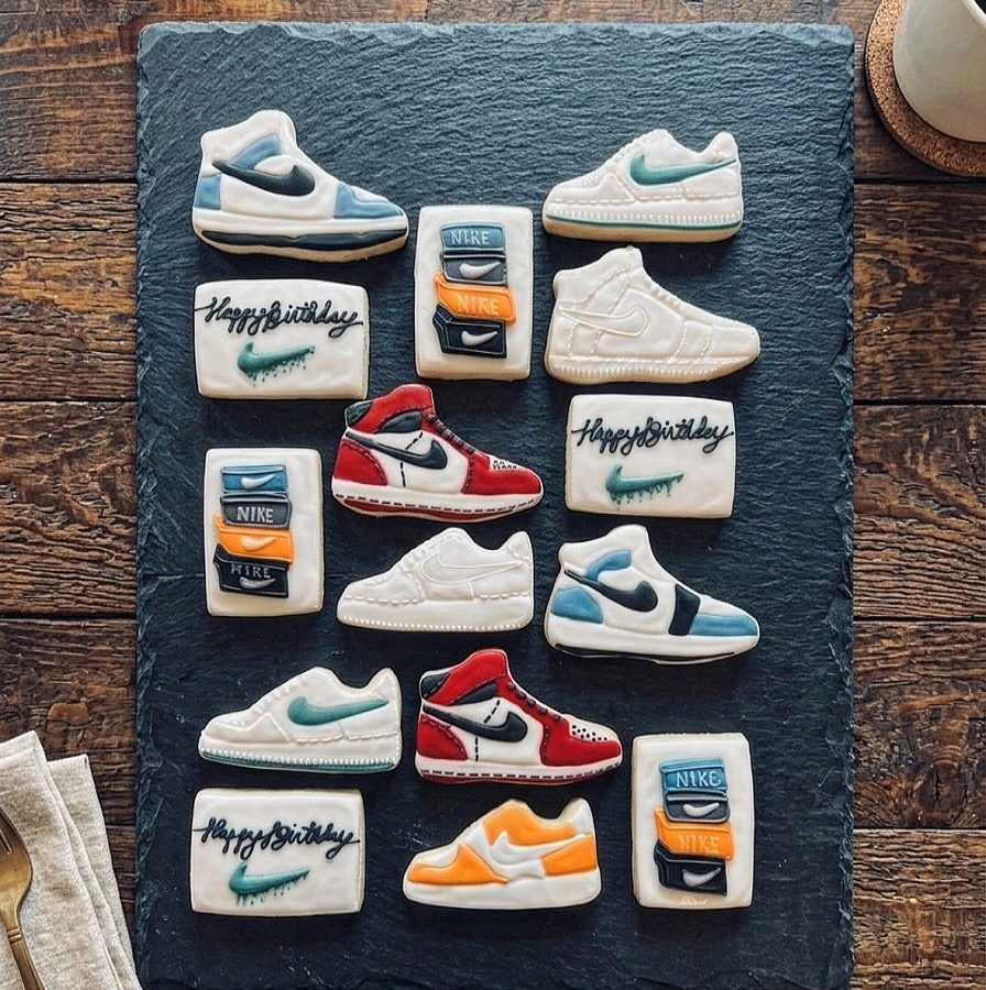 Decorated sugar cookies shaped like sneakers and shoeboxes on a slate board.