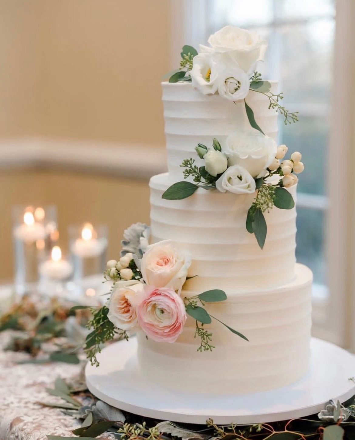 A three-tier white buttercream wedding cake with fresh roses and eucalyptus.